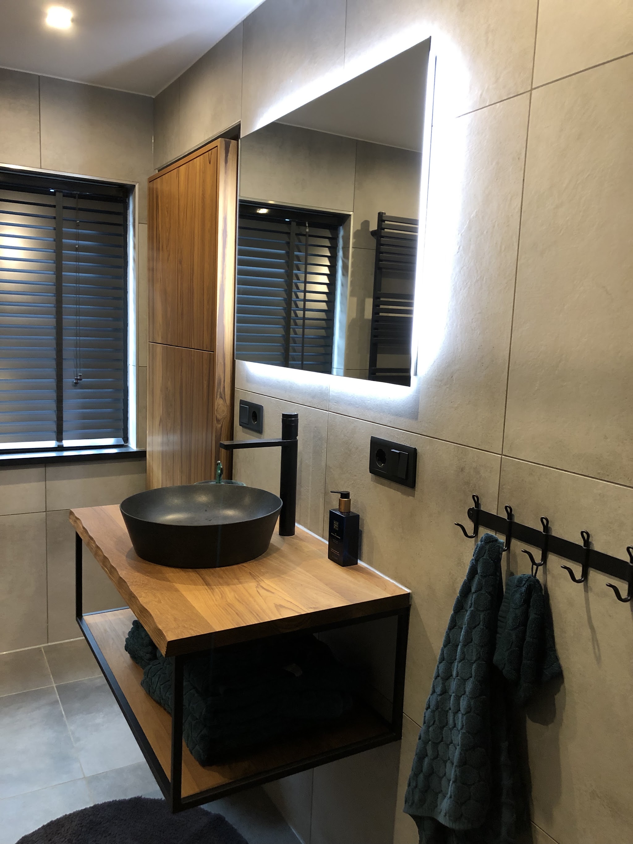 Badkamer met zwarte opzetwaskom op een eiken meubel en een spiegel met verlichting