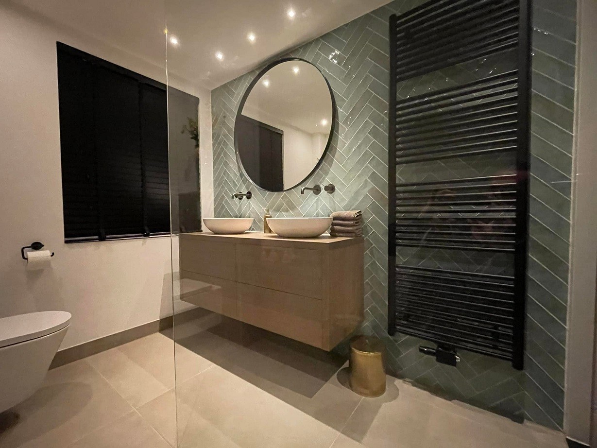 Lange badkamer met houtlook tegels, bad en een verticale strook mozaïek