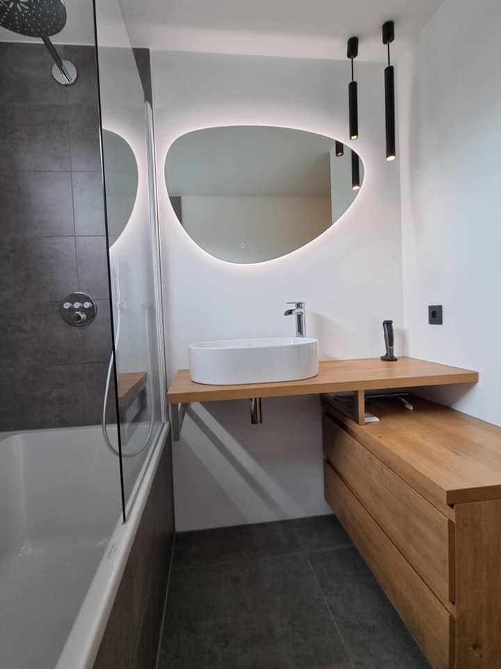 Badkamer met eiken wastafelmeubel, spiegel met verlichting en bad met glazen wand