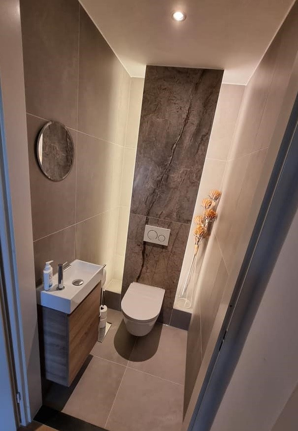 Toilet in Breda met een wand in marmerlook en ronde spiegel